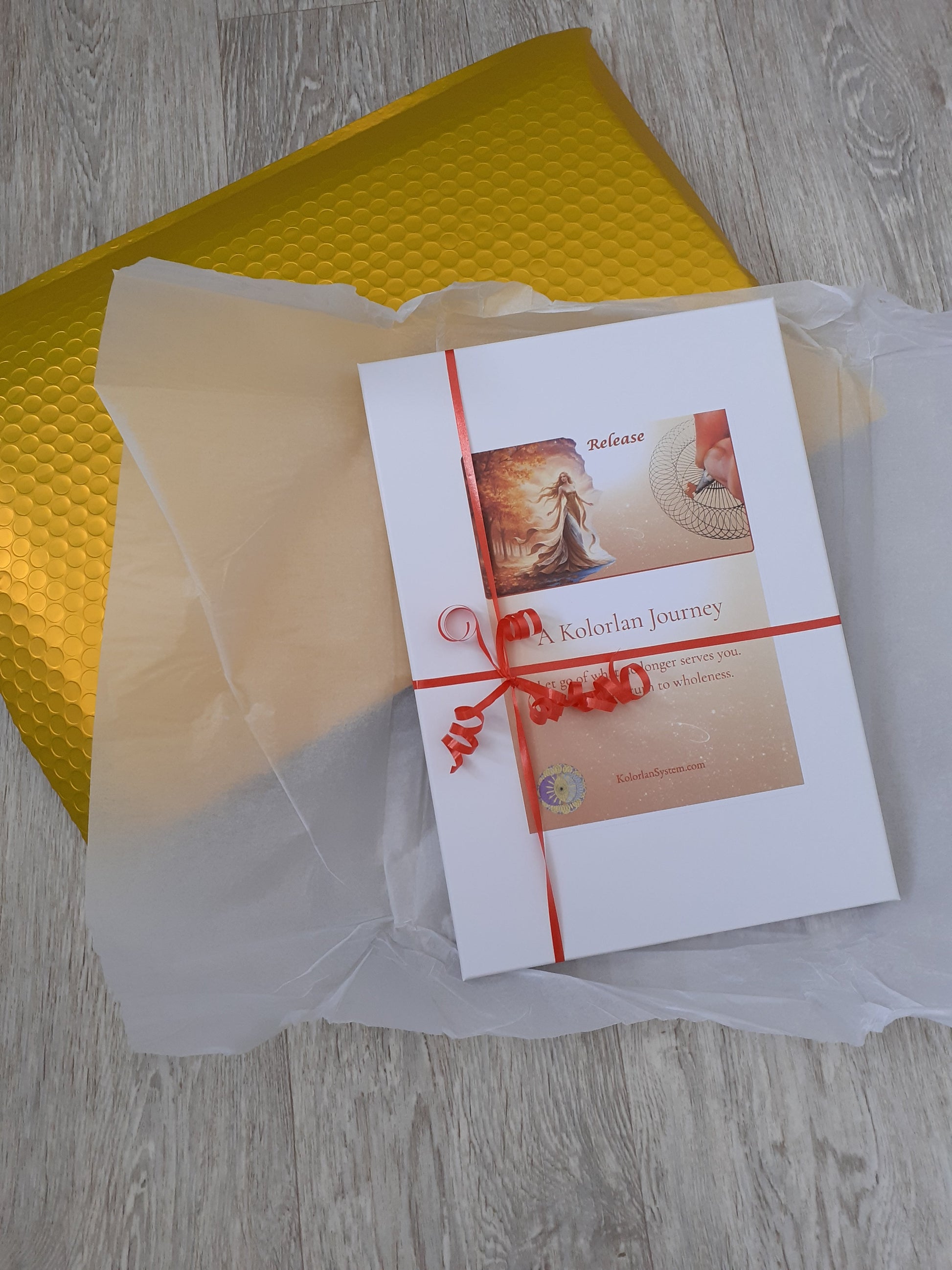 A gift wrapped box sits on a beautiful gold envelope. The box contents are a surprise, a gift for the participants of the Kolorlan journey